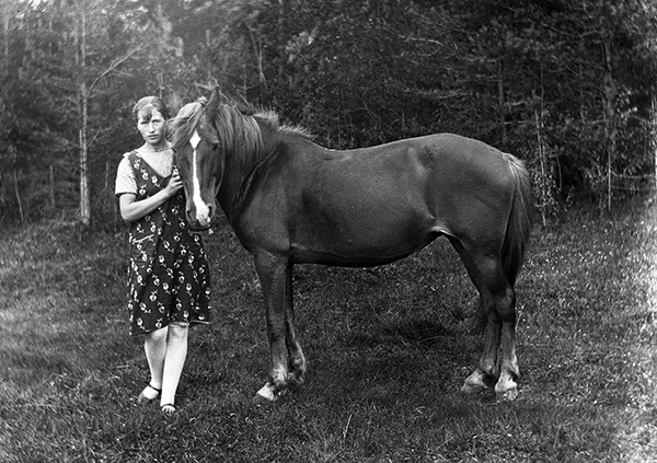 Ung kvinna stående vid häst