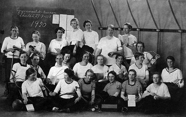 Grupp unga kvinnor i gymnastikkläder med bollar och redskap.