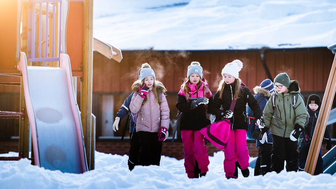 En bild som visar fyra barn som är ute på vintern. De står vid en klätterställning. Man ser att det är kallt ute på deras utandning. 